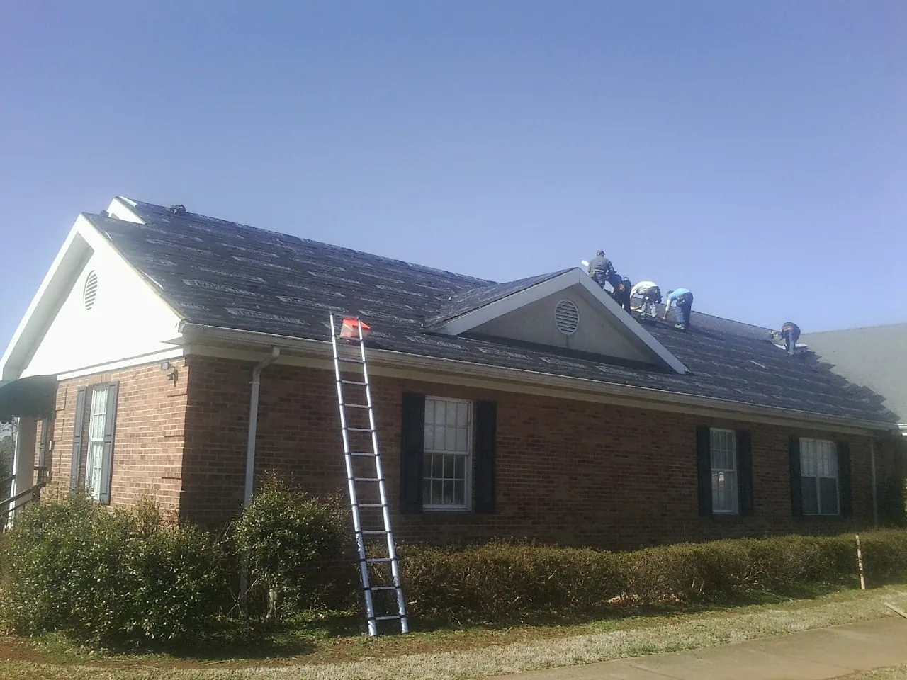 Crew tearing shingles off a brick ranch roof with a ladder set — Metal Roof Repair work by our crew in Skaneateles