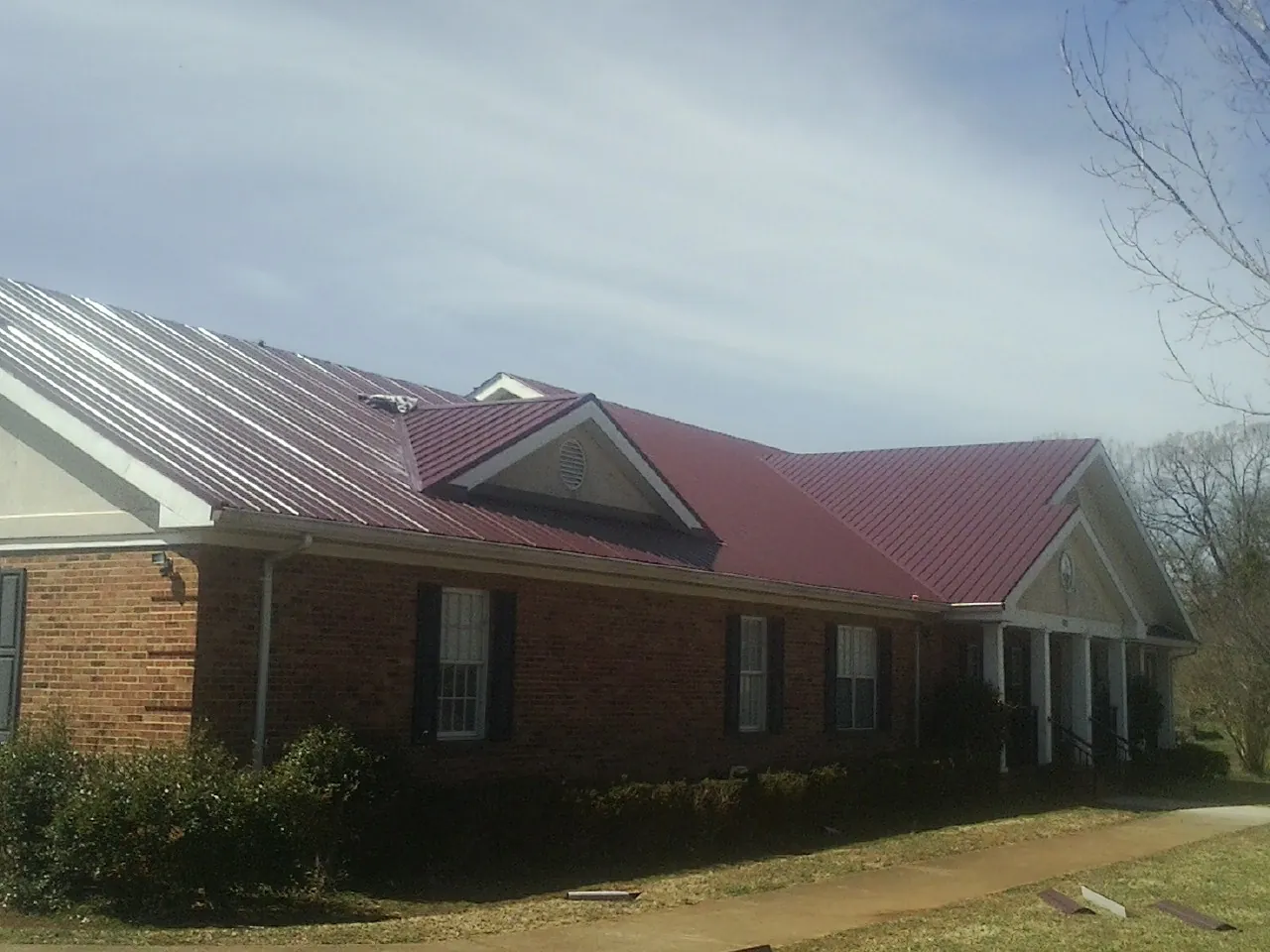 Red metal roof with gabled entries on a long brick building, from a Hail Damage Roof Repair job in Skaneateles