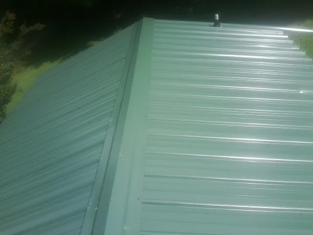 New green metal panels meeting at the ridge of a roof — Flat Roof Repair work by our crew in Skaneateles