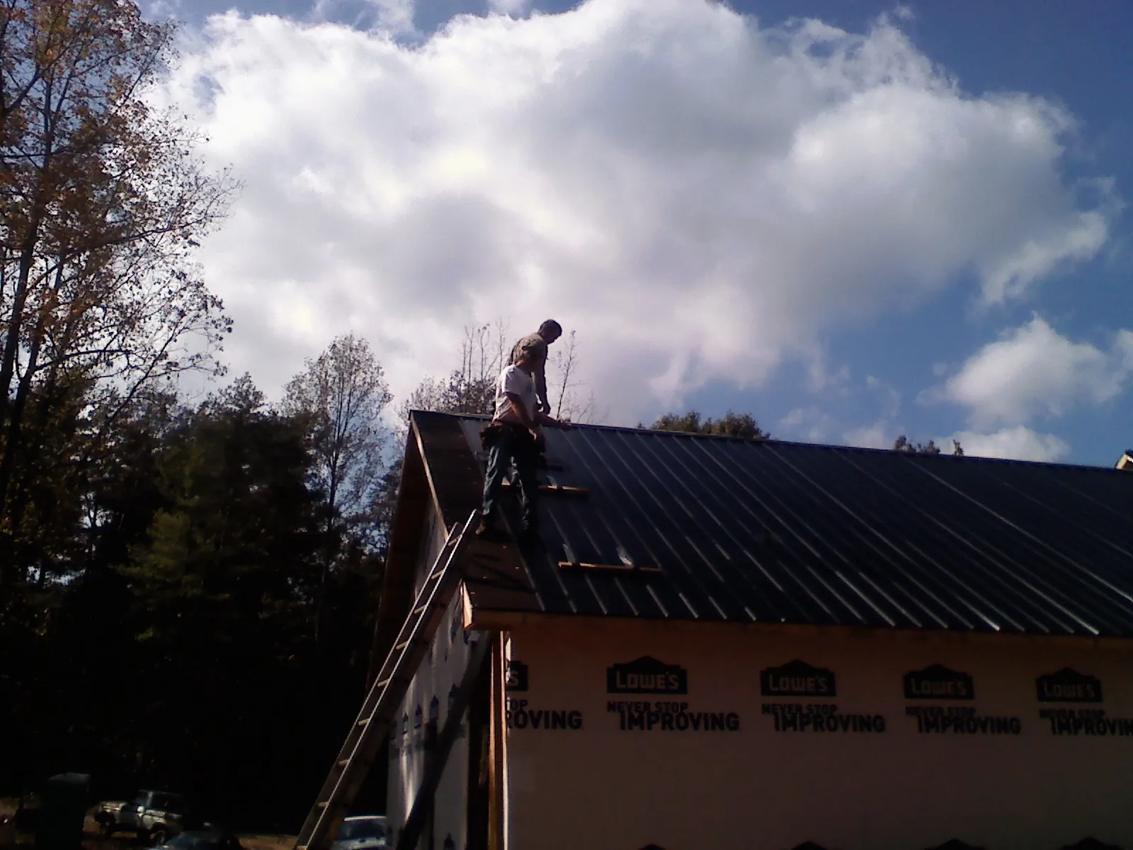 Roofer fastening dark metal panels high against a cloudy sky, from a Roof Inspection job in Skaneateles