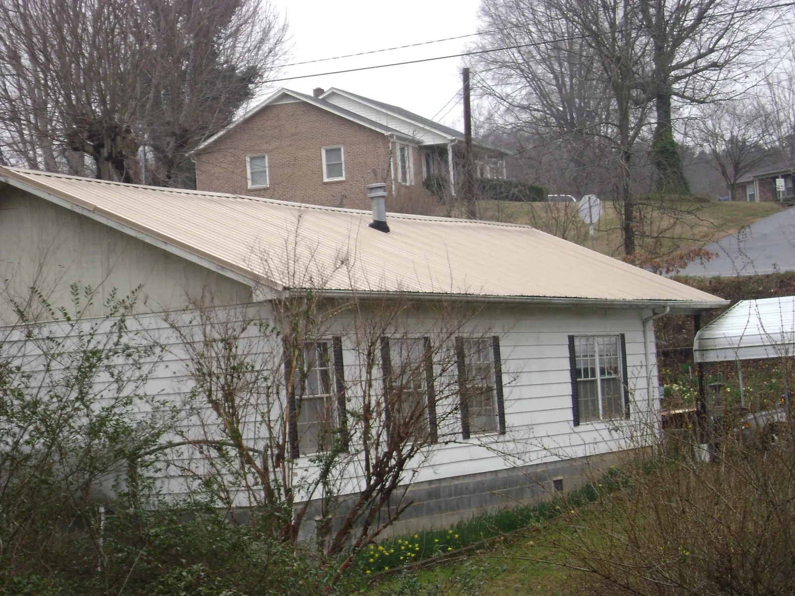 Tan metal roof on a white sided house set into a hillside — Commercial Roofing by Roofing Brothers in Skaneateles