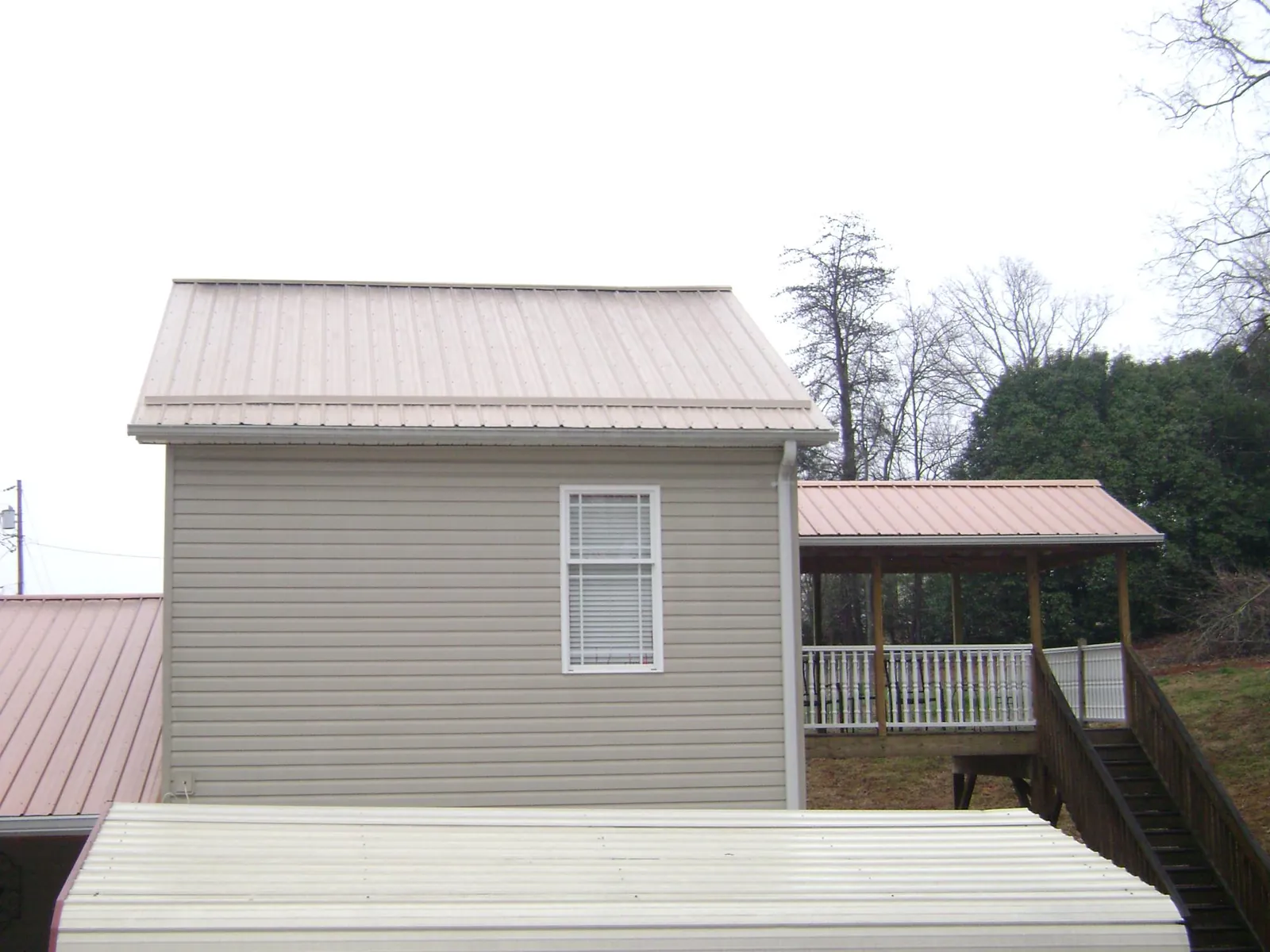 Tan metal roofs on a two story addition and attached porch, from a Roof Replacement job in Skaneateles